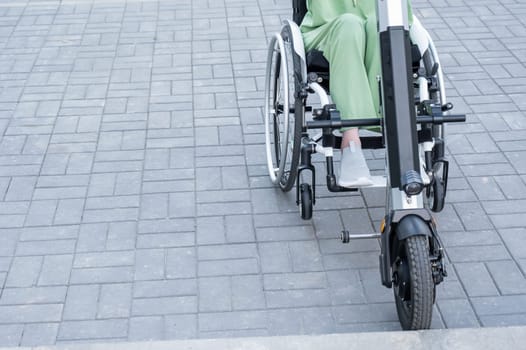 A faceless woman in a wheelchair with an assistive device for manual control. Electric handbike