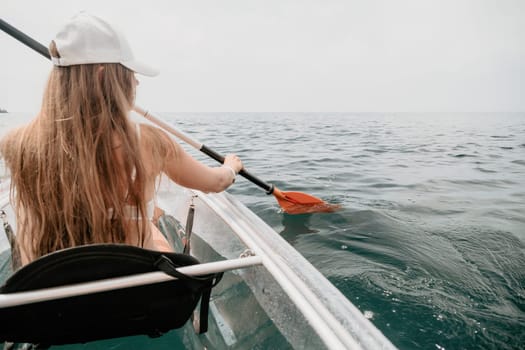 Woman in kayak back view. Happy young woman with long hair floating in transparent kayak on the crystal clear sea. Summer holiday vacation and cheerful female people having fun on the boat.