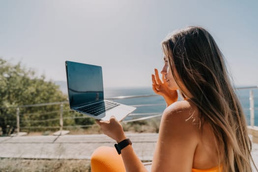 Digital nomad, Business woman working on laptop by the sea. Pretty lady typing on computer by the sea at sunset, makes a business transaction online from a distance. Freelance, remote work on vacation