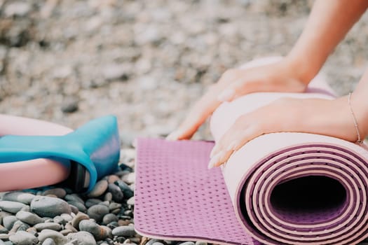 Young woman with long hair in white swimsuit and boho style braclets practicing outdoors on yoga mat by the sea on a sunset. Women's yoga fitness routine. Healthy lifestyle, harmony and meditation