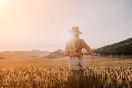 Woman farmer walks through a wheat field at sunset, touching green ears of wheat with his hands. Hand farmer is touching ears of wheat on field in sun, inspecting her harvest. Agricultural business.