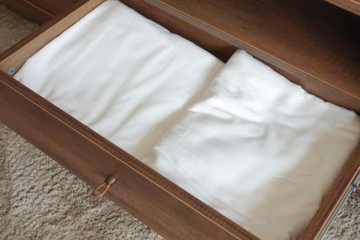 A rectangular wooden drawer on the floor contains two white linens. The hardwood plywood has a wood stain and varnish, with a patterned design
