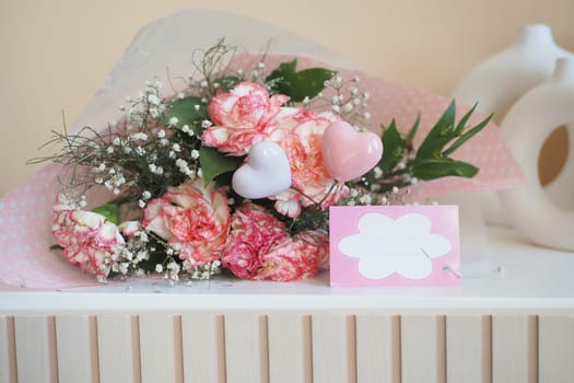 A rectangle bouquet of pink roses, hearts, and babys breath is displayed on a table alongside a card, perfect for a wedding ceremony