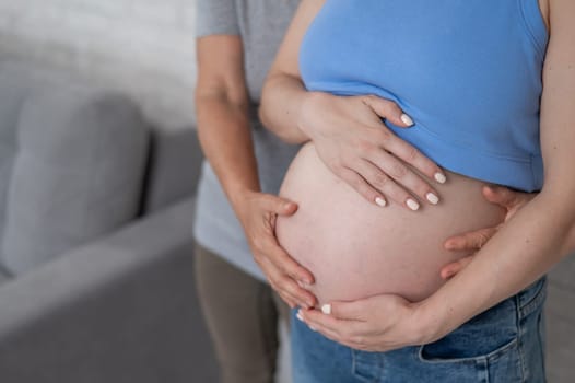 An elderly woman touches the belly of her pregnant daughter. Close-up