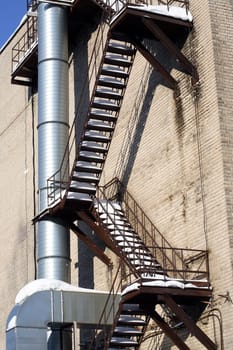 Brick wall of old factory with fire escape and metal chimney