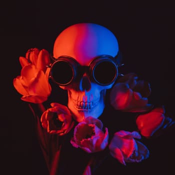 human skull in steampunk glasses in tulip flowers with red and blue neon light on a dark background. Concept of celebrating a traditional Mexican holiday of Dia De Los Muertos