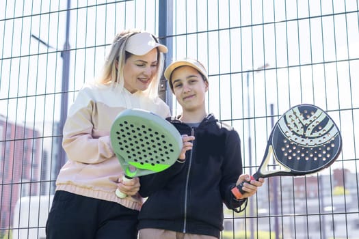 positive mother and daughter standing on court with padel rackets. High quality photo