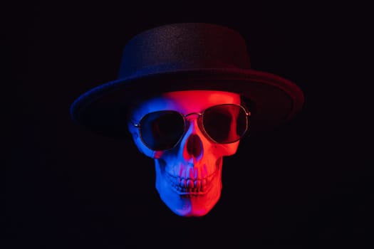 human skull wearing sunglasses and a hat with colored neon light on a dark background