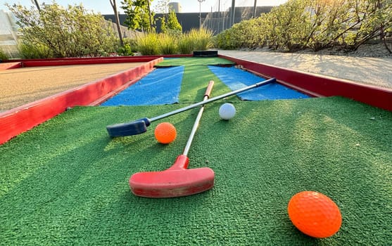 Mini-golf clubs and balls of different colors laid on artificial grass. High quality photo