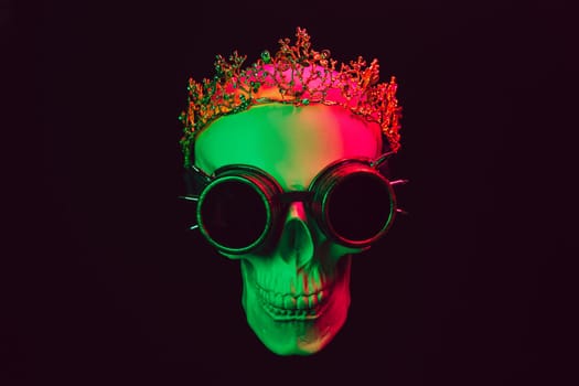human skull in a crown and steampunk glasses with colored pink green neon light on a black background