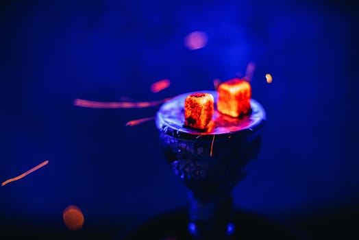 Hot coals on the bowl of the hookah with sparks for a traditional Eastern relaxation and enjoyment on a blue blurred background