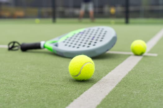 Yellow balls on grass turf near padel tennis racket behind net in green court outdoors with natural lighting. Paddle is a racquet game. Professional sport concept with copy space. High quality photo