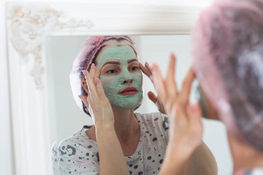 woman use a facial mask. She is looking in the mirror. High quality photo