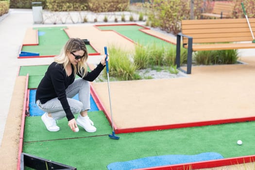 Woman playing mini golf and trying putting ball into hole. Summer leisure activity. High quality photo