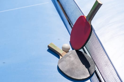 Two table tennis or ping pong rackets and ball on blue table with net. High quality photo