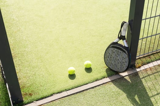 Padel racket and padel ball on a green court in the sunset. High quality photo