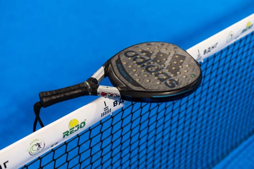 Kyiv, Ukraine, April 18, 2024. Black professional paddle tennis racket and ball with natural lighting on blue background. Horizontal sport theme poster, greeting cards, headers, website and app. High quality photo