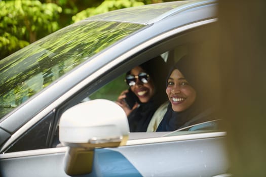 Two Muslim women wearing hijab converse on a smartphone while traveling together in a car through the.