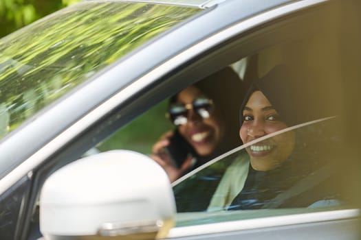 Two Muslim women wearing hijab converse on a smartphone while traveling together in a car through the.