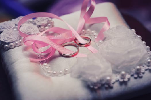 gold wedding rings on pillow with pink ribbon