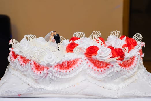 white wedding cake with red flowers cream and puppets of the bride and groom
