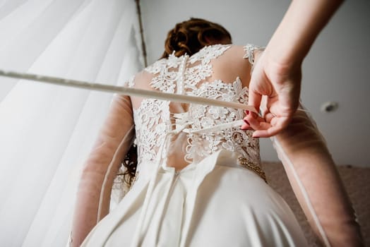 bridesmaid helps to tie ribbon on a white elegant wedding dress with lace