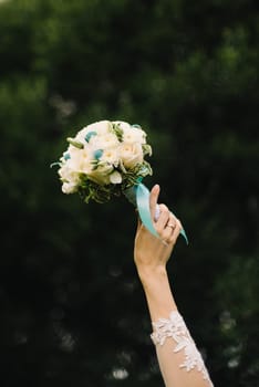 wedding bouquet of white roses in the bride's hand on green background