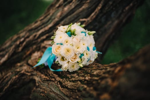 wedding bouquet of white roses with blue ribbon is on the tree
