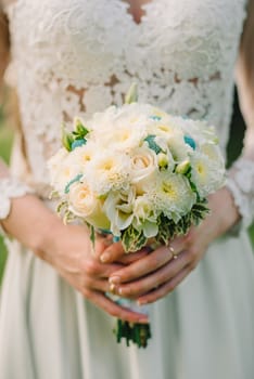 wedding bouquet of white roses in hands of bride in wedding dress