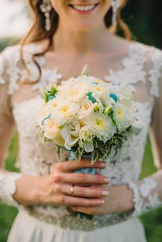 wedding white bouquet of roses in the hands of a happy bride in elegant white wedding dress