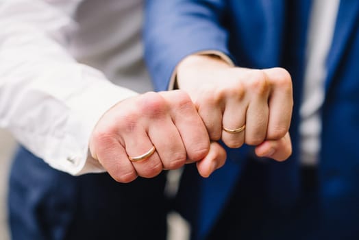 hands of two men with wedding gold rings in the shape of a fist