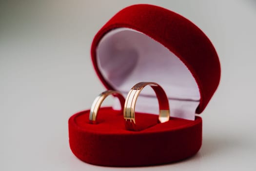 gold wedding rings symbolizing love in red box as heart on white background