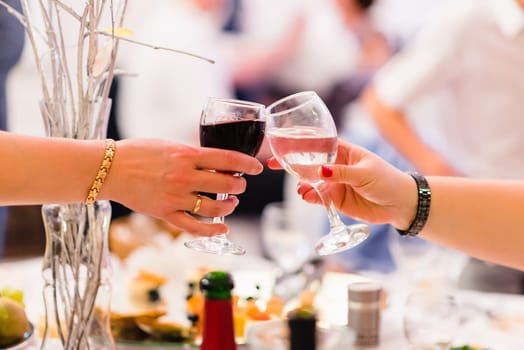 women's hands with glasses of red and white wine, clink glasses and celebrate