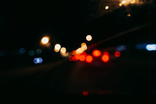 blurred city lights and red bokeh through the glass of the car on the road at night