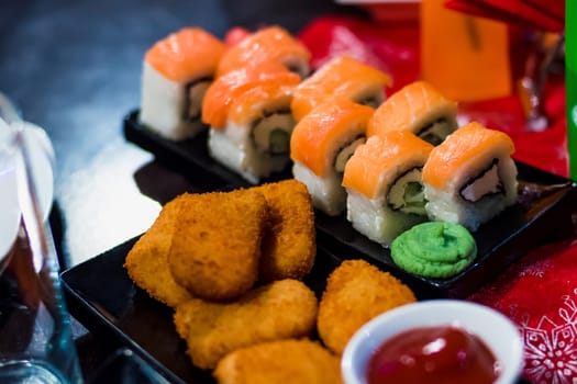 rolls with fish on a plate with sauce and chicken nuggets on the table