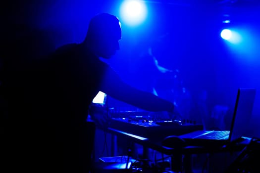 DJ plays in night club at the event under the blue lights in the headphones silhouette