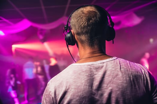 head of a DJ with headphones playing at the event in a nightclub with bright pink lighting