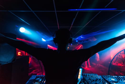 DJ in headphones waving his arms at the party night club silhouette with colored light