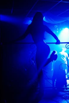 slender silhouette of a dancer in a nightclub on stage with blue illumination from the back
