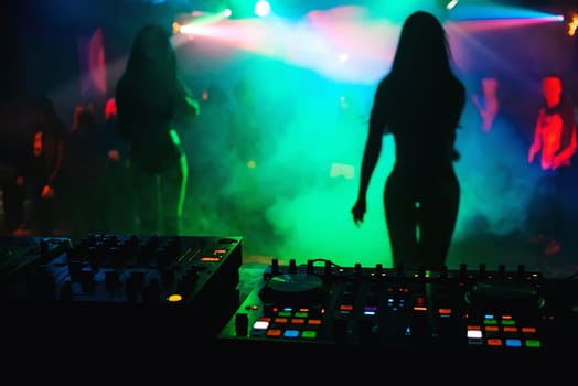 silhouette girls dancers on stage in a nightclub on the background music the mixer DJ with colorful light