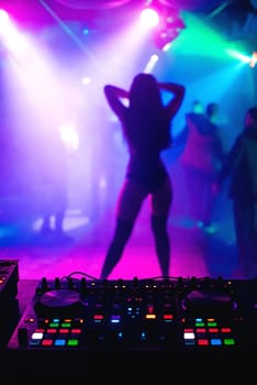 blurred silhouette of a slender girl dancer on the nightclub scene on the background mixer DJ