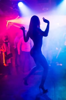 blurred silhouette of slender sexy beautiful dancers moving on the dance floor of a night club with bright lights