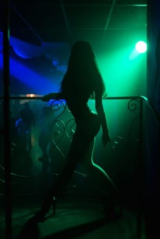 young girl with a slim sexy figure posing in a nightclub in heels with long hair silhouette