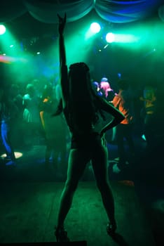 silhouette of a dancer in a night club on the dance floor with a slim sexy figure from the back with green backlight
