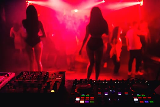 music equipment DJ mixer in night club with blurred silhouettes of girls dancers