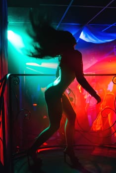 silhouette of a sexy slim slender girl on the dance floor of a nightclub dancer on stage waving hair