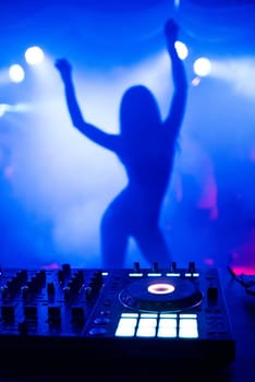 silhouette of young slim dancers on the stage ane of focus in night club with DJ mixer with blue background