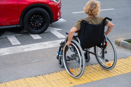 Rear view of an elderly Caucasian woman in a wheelchair crosses the road at a pedestrian crossing