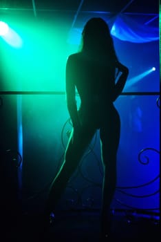 silhouette of a slender young girl dancer posing on stage with green and blue backlight