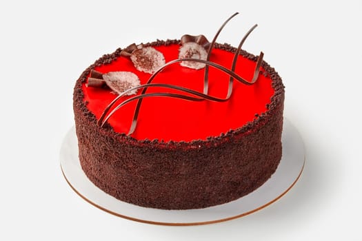Elegant chocolate cake with vibrant red glaze and decorative chocolate shavings, presented on white background. Traditions of confectionery art